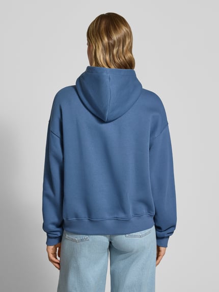 Frauenmodel trägt Hoodie mit Känguru-Tasche von Gina Tricot in Blau, Baumwoll-Mix, Relaxed Fit, Ganzkörperansicht Rückansicht.
