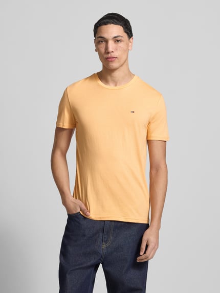Männermodel trägt Slim Fit T-Shirt aus Baumwoll-Mix Modell 'JASPE HERITAGE' von Tommy Jeans in Melange-Optik mit Logo-Stitching, Ganzkörperansicht von vorne.