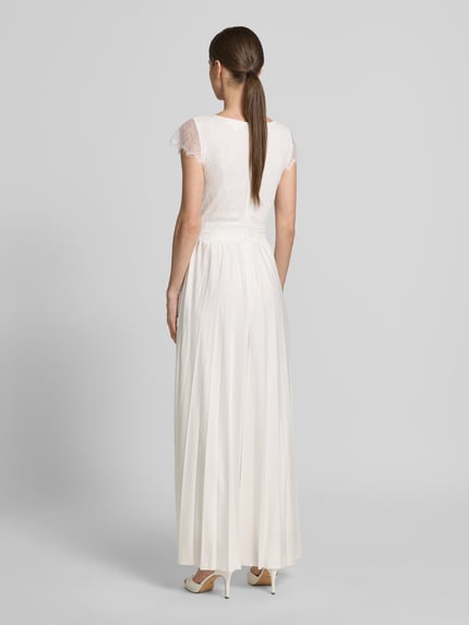 Vrouwenmodel draagt Braut-Jumpsuit met diep V-hals model 'Emmie' van GUIDO MARIA KRETSCHMER WOMAN in recht fit, top van kant, plooien rok, witte kleur, detailrits achter, tailleband, gladde textuur, ruglengte 135 cm bij maat 36, volledige lichaamsaanzicht achterkant.