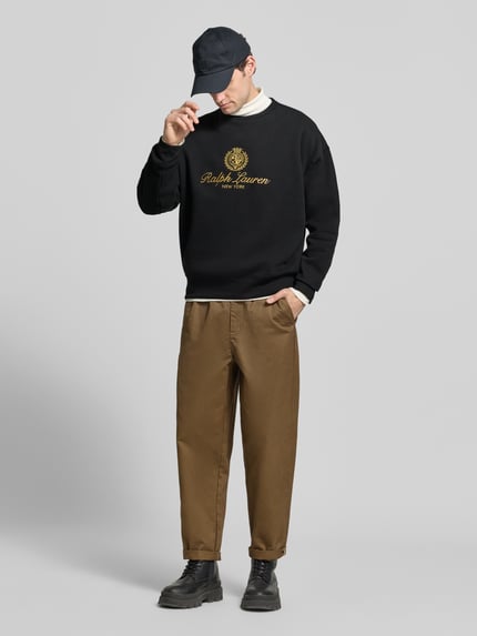 Männermodel trägt Sweatshirt mit Logo-Print von POLO RALPH LAUREN in Schwarz, Baumwollmix, unifarben mit Motiv-Print, Ganzkörperansicht von vorne.