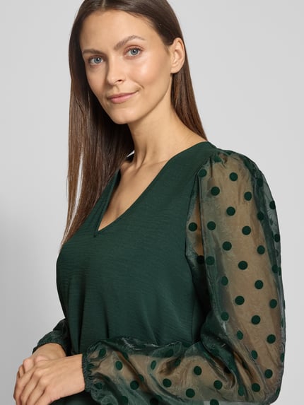 Frauenmodel trägt Fließendes Cocktailkleid mit semitransparenten Ärmeln Modell 'ALVA' von Vero Moda, Optik: Unifarben, Passform: Fließend, Mini-Länge, V-Ausschnitt, Ballonärmel mit elastischem Ärmelabschluss, Materialverarbeitung: Crinkle, Dunkelgrün, semitransparente gepunktete Ärmel, Nahaufnahme Oberkörper.