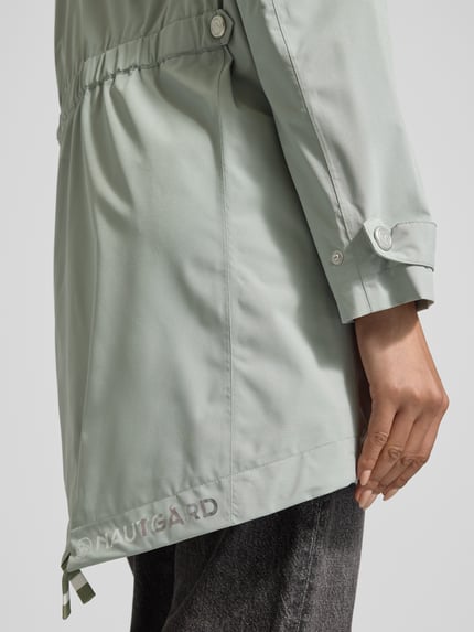 Kobiece modelka nosi 'Jacke mit Ärmelriegeln' od NAUTGÅRD, krój regular fit, materiał jasnoszary, detal rękawa i logo, zbliżenie bok.