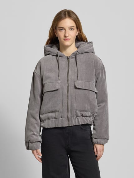 Frauenmodel trägt Regular Fit Bomberjacke mit Kapuze Modell 'SUVA' von Only, grau, Cord, aufgesetzte Taschen, Ganzkörperansicht von vorne.