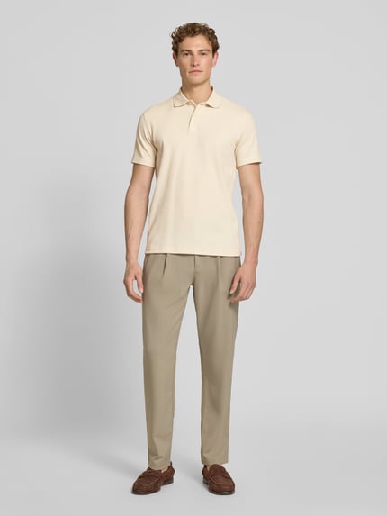 Mężczyzna model nosi Regular Fit Poloshirt aus Baumwoll-Mix Modell 'BLAZE' od SELECTED HOMME, piqué, jednokolorowy, krój regular fit, krótki rękaw, polokrag, V-dekolt, beżowy, widok całej sylwetki od przodu.