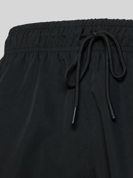 Produktfoto, schwarze Badeshorts mit Logo-Stitching von Lacoste, elastischer Bund, Tunnelzug, seitliche Taschen, glatte Textur, schnelltrocknend.