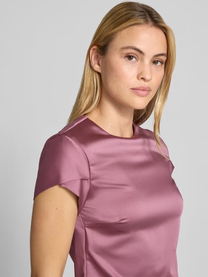 Frauenmodel trägt Bluse aus Satin von Rinascimento in Rosa mit Rundhalsausschnitt, Material-Mix, Kurzarm, Nahaufnahme Oberkörper.