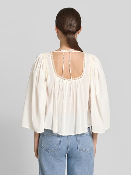 Frauenmodel trägt Cropped Bluse mit 3/4-Arm Modell 'ISMARA' von Drykorn aus Baumwoll-Viskose-Mix in Creme, Rückenlänge 35 cm, Ganzkörperansicht Rückansicht.