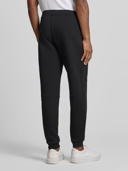 Männermodel trägt schwarze Sweatpants mit Viskose-Anteil Modell 'TRAIN PREMIUM SHIELD' von EA7 Emporio Armani, Gerade Passform, Rückansicht.