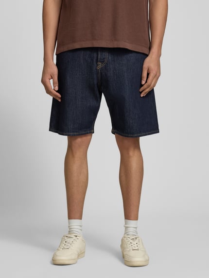 Männermodel trägt Relaxed Fit Jeansshorts Modell 'TONY' von Jack & Jones aus dunkelblauem Baumwoll-Elasthan-Mix mit Eingrifftaschen, Ganzkörperansicht von vorne. Bundweite bei Größe M: 42 cm, Innenbeinlänge: 21 cm.