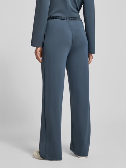 Frauenmodel trägt Sweatpants mit elastischem Bund und Eingrifftaschen von Scotch & Soda im Material-Mix mit Modal-Anteil in Blau, weites Bein, Innenbeinlänge 80 cm in Größe S, Ganzkörperansicht Rückansicht.