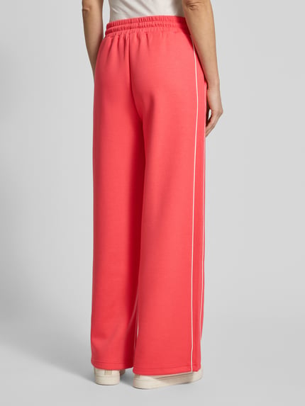 Frauenmodel trägt Wide Fit Sweatpants mit elastischem Bund Modell 'KATE NEO' von ICHI in Koralle, weiche Textur, Ganzkörperansicht Rückansicht. Material-Mix mit Viskose-Anteil und Tunnelzug, Kontrastpaspelierung sichtbar.