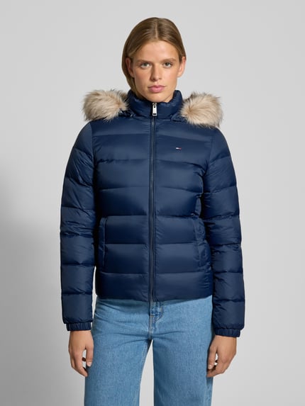 Frauenmodel trägt Regular Fit Daunenjacke mit Kunstfell von Tommy Jeans in Dunkelblau mit Fellkapuze und Reißverschluss, Ganzkörperansicht von vorne. Damen Daunenjacke von Tommy Jeans.