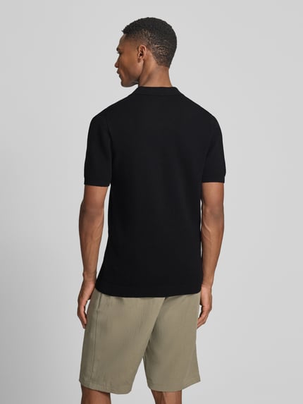 Männermodel trägt Slim Fit Poloshirt Modell 'Triton' von Drykorn aus reiner Baumwolle mit Polokragen, Strukturmuster, Rückenlänge 67 cm, Ganzkörperansicht Rückansicht.