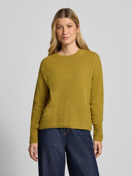 Kobiece modelka ma na sobie Strickpullover mit überschnittenen Schultern od Christian Berg Woman, luźny krój, prążkowane wykończenia, okrągły dekolt, długie rękawy, długość z tyłu w rozmiarze M: 60 cm, długość rękawa: 58 cm, kolor musztardowy, prosty fason, gładka tekstura, pełny widok z przodu.