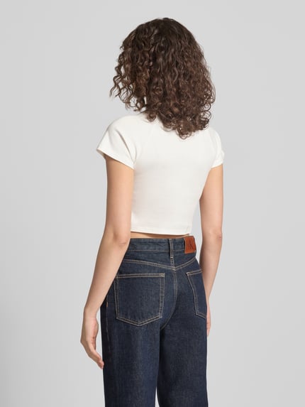 Modelka prezentuje Cropped T-Shirt mit Logo-Print von ANOTHER COTTON LAB, bawełna, krój krótki, nadruk z logo, okrągły dekolt, długość tyłu w rozmiarze S: 36 cm, widok całej sylwetki z tyłu.