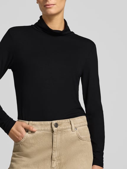 Frauenmodel trägt Slim Fit Longsleeve aus Viskose-Mix Modell 'Liana' von FREE/QUENT in Schwarz, glatte Textur, Nahaufnahme Oberkörper. Damen Longsleeve mit Stehkragen, Rückenlänge bei Größe S 60 cm, Viskose-Elasthan-Mix.