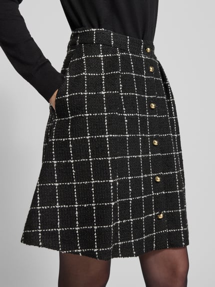 Männermodel trägt Ausgestellter Mini-Rock mit Viskose-Anteil Modell 'RIKLA-1' von HUGO, czarny bouclé z wzorem kratki, guziki, mini, detal boczny, ujęcie z przodu, z kontekstem eleganckiej mody damskiej