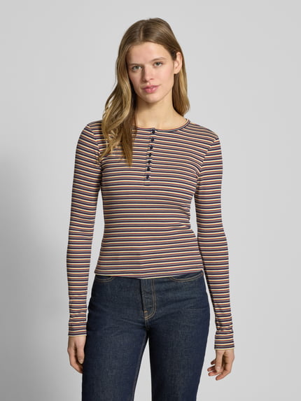 Kobiece modelka nosi Slim Fit Longsleeve mit Knopfleiste od REVIEW, mieszanka bawełny, krój slim fit, okrągły dekolt, listwa guzikowa, długość tyłu w rozmiarze S: 50 cm, wielokolorowe paski, tekstura gładka, widok całej sylwetki z przodu.