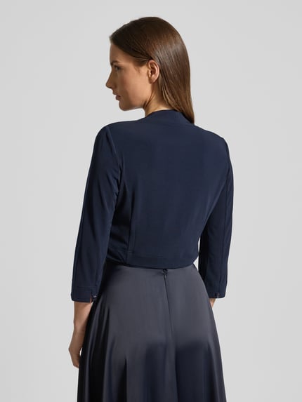 Frauenmodel trägt Bolero mit offener Vorderseite von VM Vera Mont, dunkelblauer Material-Mix mit Stretch-Anteil, Gerader-Schnitt, Sportmanschetten, Rückenlänge bei Größe 36: 42 cm, Ganzkörperansicht Rückansicht.