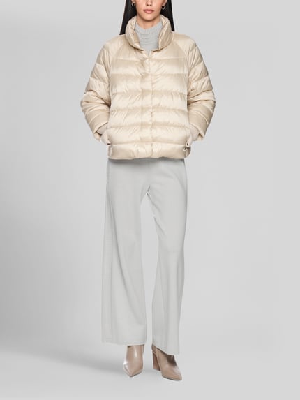 Frauenmodel trägt Steppjacke mit Stehkragen und Label-Detail von Marc Cain in Beige, strukturierte Oberfläche, Eingrifftaschen, Ganzkörperansicht von vorne. Rückenlänge 56 cm, Schulterbreite 41 cm, Brustweite 55 cm, Ärmellänge 73 cm, Regular Fit.