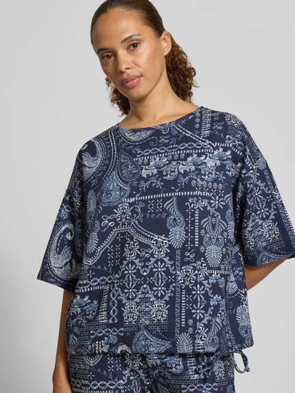 Kobiece model prezentuje Relaxed Fit Bluse aus Viskose-Mix von Christian Berg Woman, ciemnoniebieska mieszanka wiskozy, wzór paisley na całej powierzchni, okrągły dekolt, rękaw o dł. 1/2, tkanina o miękkiej teksturze, Ganzkörperansicht z przodu.