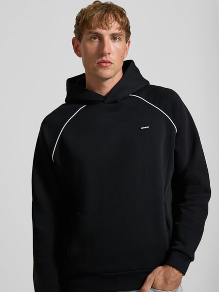 Männermodel trägt Hoodie mit Logoprint und Kontrastspipings von REVIEW, Baumwoll-Mix, Regular Fit, schwarze Farbe, Nahaufnahme Oberkörper.