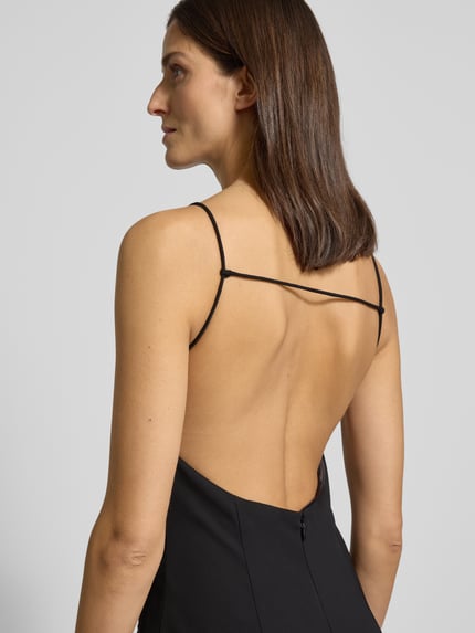 Frauenmodel trägt Jumpsuit mit Eingrifftaschen von Mango, schwarzer Stoff, Spaghettiträger, lockerer Schnitt, Detailaufnahme Rückenansicht.