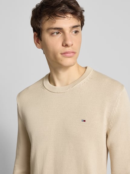 Männermodel trägt Regular Fit Strickpullover aus reiner Baumwolle van Tommy Jeans, beige, unifarben, logo detail, Nahaufnahme Oberkörper.