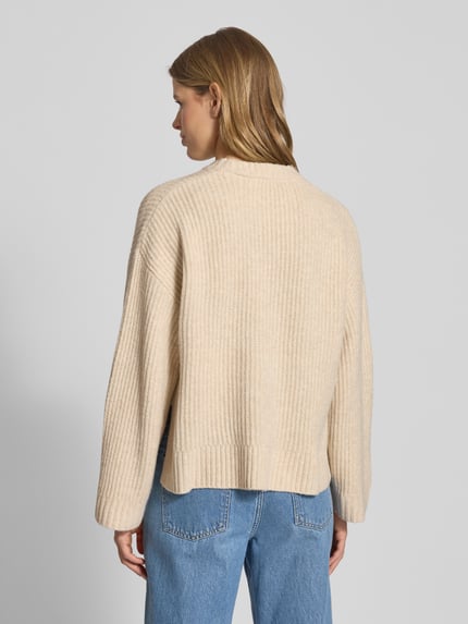 Vrouwenmodel draagt oversize gebreide trui met geribde boorden, model 'SIGGA' van JJXX, beige tint, materiaal met wolmix, rugaanzicht.