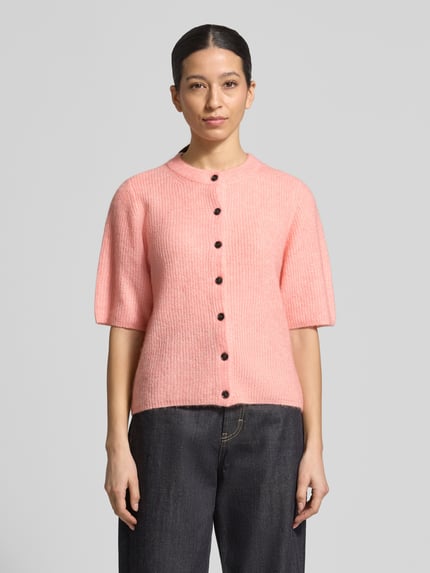 Frauenmodel trägt Strickjacke mit Woll-Anteil Modell 'Jinie Hope' von MSCH Copenhagen in Rosa, Material-Mix, Gerader-Schnitt, Rundhalsausschnitt, Knopfleiste, 1/2-Arm, Rückenlänge 56 cm, Ärmellänge 32 cm, Ganzkörperansicht von vorne.