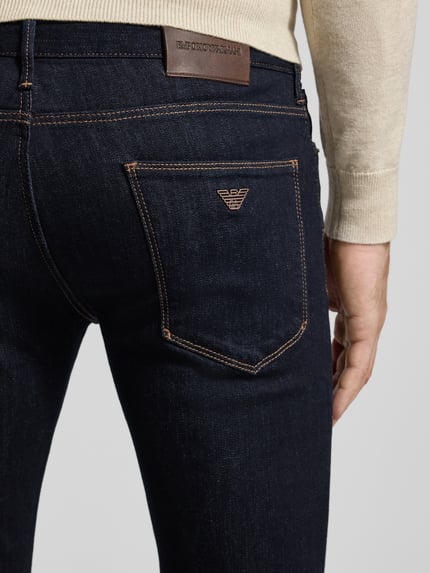 Männermodel trägt Slim Fit Jeans mit Logo-Applikation von Emporio Armani, dunkler Denim, 5-Pocket-Design, Detailaufnahme Rückansicht.