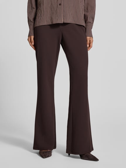 Männermodel trägt High Waist Bootcut Hose mit Knopf- und Reißverschluss von MICHAEL Michael Kors, materiał z domieszką stretchu, krój bootcut, kieszenie z tyłu, szerokość w rozmiarze S: 38 cm, długość wewnętrzna nogawki w rozmiarze S: 82 cm, ciemny brąz, gładka tekstura, Ganzkörperansicht von vorne