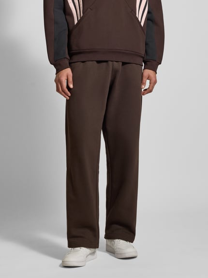 Mężczyznamodel nosi Straight Fit Sweatpants mit Logo-Stitching od adidas Originals, bawełna, elastyczny pas, widok całej sylwetki z przodu.
