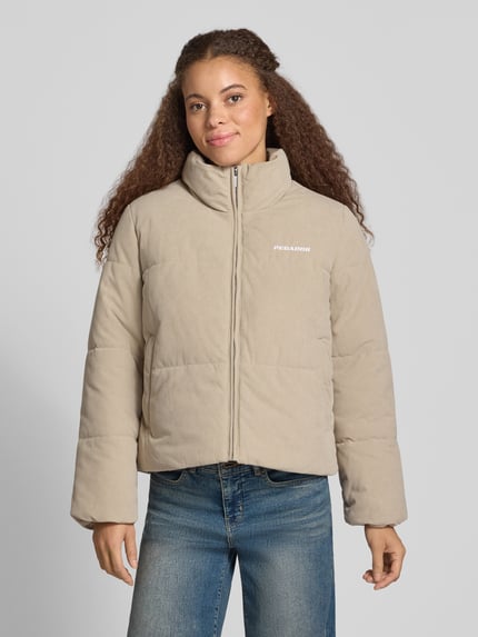 Frauenmodel trägt Relaxed Fit Steppjacke in Cord-Optik von PEGADOR w beżowym kolorze, wyhaftowane logo, stójka, imitacja sztruksu, długość tyłu w rozmiarze S: 58 cm, szerokość ramion w rozmiarze S: 42 cm, szerokość w rozmiarze S: 57 cm, długość rękawów w rozmiarze S: 61 cm, widok całej sylwetki z przodu.