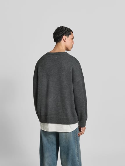 Męski model trägt Oversized Pullover aus Woll-Mix von MM6 Maison Margiela w kolorze ciemnoszarym, krój oversized fit, imitacja dzianiny, wyhaftowane logo, okrągły dekolt, długość tyłu w rozmiarze M: 80 cm, Ganzkörperansicht Rückansicht.
