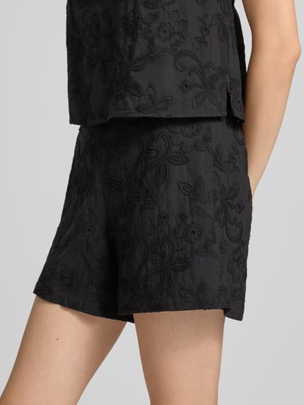 Frauenmodel trägt Regular Fit Stoffshorts aus reiner Baumwolle Modell 'PCGINGER' von PIECES, schwarze Farbe, florales Muster, Nahaufnahme Oberschenkel, Damen Stoffshorts von PIECES