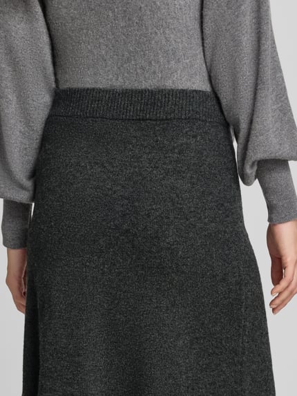Frauenmodel trägt Knielanger Strickrock mit elastischem Bund von Christian Berg Woman in dunklem Grau aus reiner Baumwolle, Nahaufnahme Rückansicht.