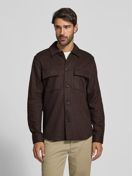 Męski model nosi Regular Fit Hemdjacke mit Kentkragen und Brusttaschen od Profuomo, brązowy materiał z domieszką wełny, przód z guzikami, kieszenie na piersi, bokserki beżowe, kontekst: kurtka męska Profuomo, mieszanka materiałów z wełną z owiec, krój regular fit, kołnierzyk kent, długość pleców w rozmiarze M: 76 cm, całopostaciowy widok z przodu.