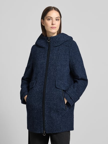 Frauenmodel trägt Mantel mit Kapuze von GIL BRET in Melange-Optik, Longline-Schnitt, Strukturmuster, Bouclé, Nahaufnahme Oberkörper.