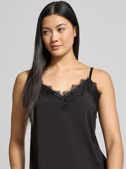 Frauenmodel trägt Trägertop mit Fransen Modell 'BICCO' von FREE/QUENT aus schwarzem Material-Mix mit Stretch-Anteil, Nahaufnahme Oberkörper.