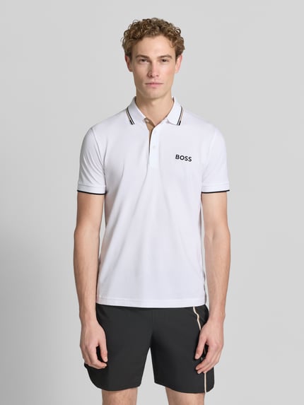 Mężczyzna nosi koszulkę polo Regular Fit model 'PADDY PRO' z mieszanki bawełny od BOSS Green, biały kolor, czarne akcenty, gładka tekstura, całkowity widok z przodu.