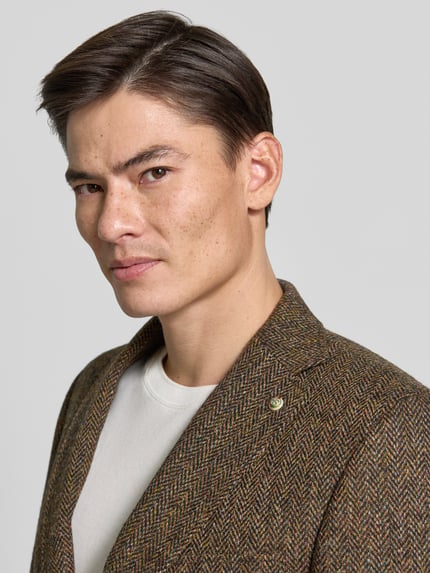 Männermodel trägt Slim Fit 2-Knopf-Sakko mit Pattentaschen Modell 'Theo' von Carl Gross aus czysta żywa wełna, Kołnierz z połami, kieszenie z patką, Ganzkörperansicht von vorne, kontekst: długość tyłu 75 cm, szerokość ramion 44 cm, długość rękawów 66 cm.