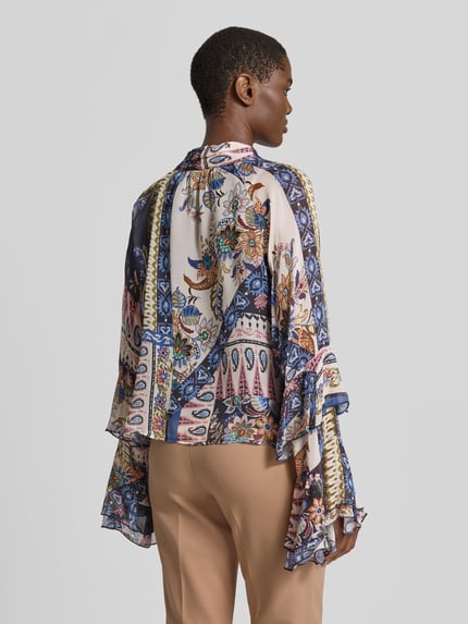 Frauenmodel trägt Schluppenbluse aus Viskose mit Volants von Milano Italy, gemustert in Beige und Blau, Kimonoärmel, Ganzkörperansicht Rückansicht.