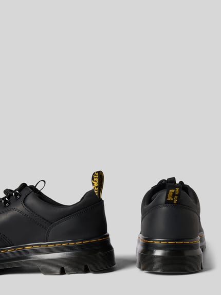 Produktfoto, Schuhe aus echtem Leder Modell 'Reeder' von Dr. Martens in Schwarz mit gelber Naht, runde Form, strukturierte Sohle, Profilsohle und Schnürverschluss, abgerundete Passform, Absatzhöhe 5 cm, Schafthöhe 7 cm, Schaftweite 8 cm.