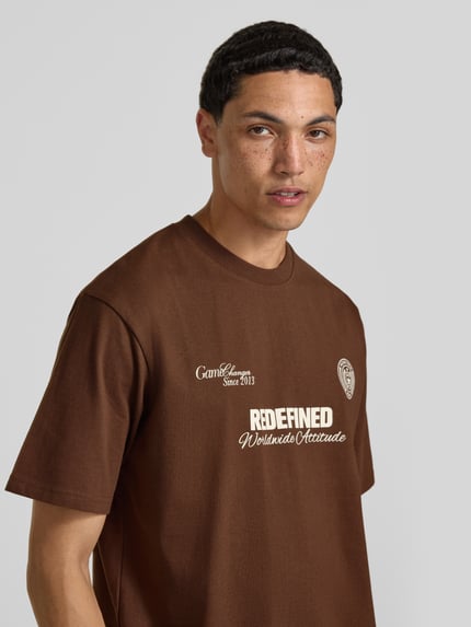 Männermodel trägt T-Shirt mit Statement-Print und Rundhalsausschnitt von Redefined Rebel, Braun, Baumwoll-Mix, Relaxed-Fit, Nahaufnahme Oberkörper.