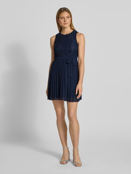 Frauenmodel trägt Knielanges Kleid mit Spitze von Apricot in Dunkelblau, Material-Mix mit Viskose-Anteil, Taillierter Schnitt, Rundhalsausschnitt, Bindegürtel, Rock mit Plisseefalten, Schlüsselloch-Ausschnitt hinten, Ganzkörperansicht von vorne.
