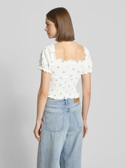 Frauenmodel trägt Slim Fit Blusentop mit Allover-Muster Modell 'HILLARY' von Only, florales Muster auf weiß, Cropped-Länge, kurzarm, Henley-Ausschnitt, ohne Kragen, Passform: Slim Fit, Ärmelabschluss mit Raffungen, Optik:Allover-Muster, Jeans, Ganzkörperansicht Rückansicht.
