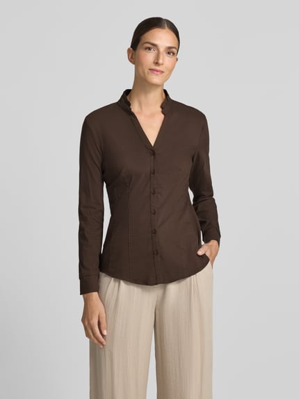 Frauenmodel trägt Bluse aus Baumwoll-Mix von MORE & MORE in Braun, taillierte Passform, Stehkragen mit Rüschen, Ganzkörperansicht von vorne.