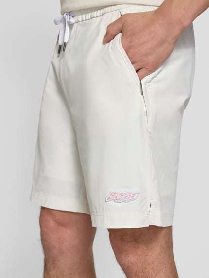 Männermodel trägt Relaxed Fit Sport-Shorts mit seitlichen Reißverschlusstaschen Modell 'Fisher' von BOSS Orange in Unifarben mit Tunnelzug, Elastisch und Reißverschlusstaschen, Nahaufnahme Oberkörper.