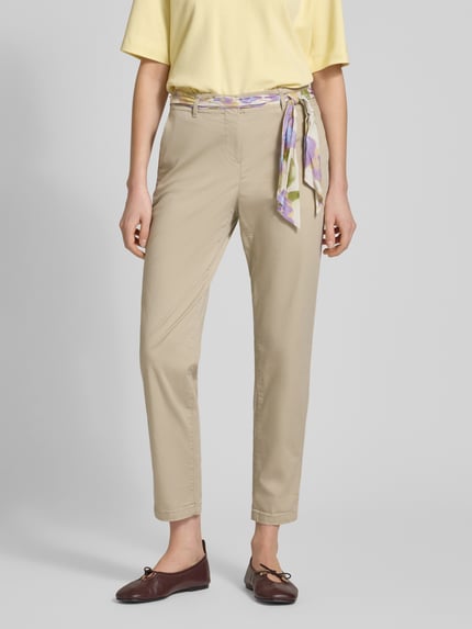 Kobiece model prezentuje Slim Fit Chino mit Viskose-Anteil od Christian Berg Woman, mieszanka bawełny i wiskozy, krój slim fit, skrócony fason, zdejmowana materiałowa tasiemka, zapięcie na guzik i zamek błyskawiczny, jasny beż, gładka faktura, przód spodni, widok całej sylwetki z przodu.